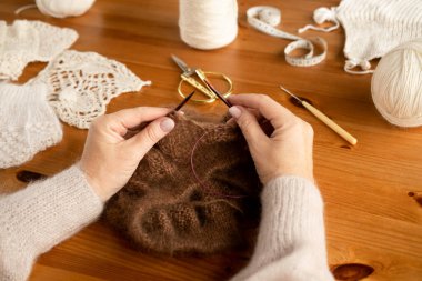 Kadının elleri yün kahverengi iplik desenleri örüyor. Resmi kapat.