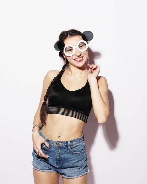 Saçları örgülü, güneş gözlüklü, beyaz arka planda gülümseyen neşeli, esmer bir kadın..