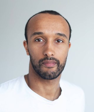 Açık gri arka planda traşsız genç bir adam. Karışık ırk yakışıklı erkek model. Portreyi kapat.