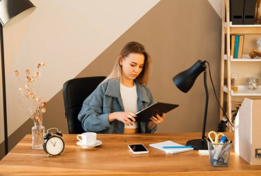 Gündelik çalışan dijital tablet giyen genç sarışın kadın. İş kadını, ev ofisteki dijital tablet üzerinde çalışıyor..