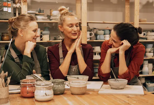 A company of three cheerful young women friends are painting ceramics in a pottery workshop. Lifestyle and people concept.