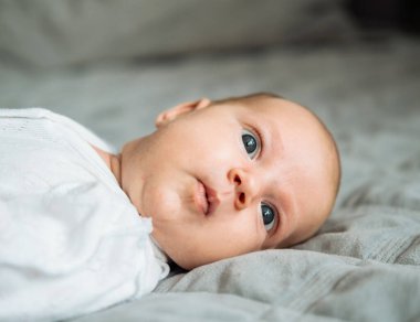 Beyaz tulumlu yeni doğmuş bebek bir battaniyenin üzerinde yatıyor. Bebek, insanlar ve çocukluk kavramı.