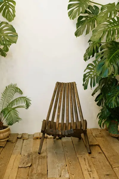 Comfortable wooden chair on wooden floor next to tropical flowers. Room for meditation and relaxation.