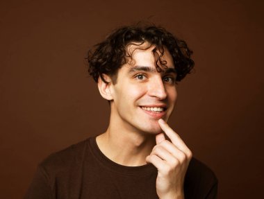 Yakışıklı genç adam kahverengi tişört giyer ve kahverengi arka planda kameraya bakar. Portreyi kapat.