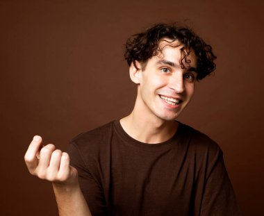 Yakışıklı genç adam kahverengi tişört giyer ve kahverengi arka planda kameraya bakar. Portreyi kapat.