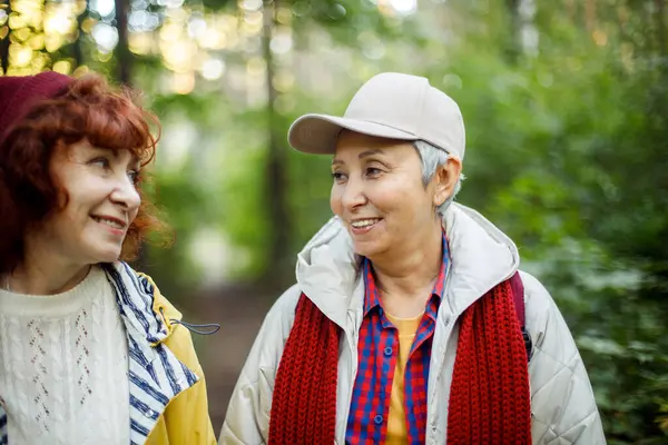 秋の公園で背が高く笑っている2人の陽気な年金女性の友人 ストック画像