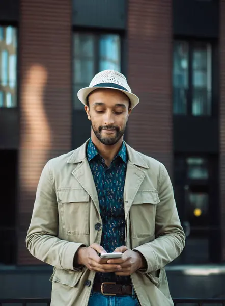 在现代商务中心附近 年轻英俊的非洲男子戴着帽子 用智能手机发短信 图库照片