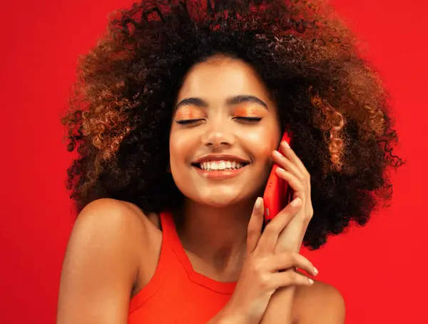 赤い背景に隔離された携帯電話で話している興奮する若いアフロアメリカの女性の肖像画 ロイヤリティフリーのストック画像