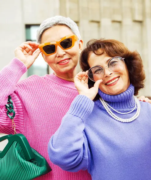 两个穿着鲜艳毛衣和太阳镜的快乐的退休女性朋友走在一起 生活方式和人的概念 图库图片