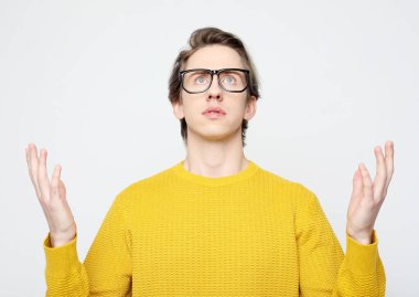 Sarı kazaklı bir adam kollarını kaldırır şaşkınlıkla, beyaz arka planda bir şaşkınlık jesti.