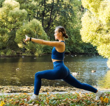 Genç sarışın kadın göl kenarındaki parkta yoga egzersizi yapıyor. Spor yoga konsepti.
