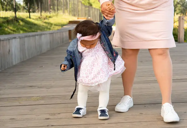 这个女婴迈出了第一步 妈妈牵着一个小女孩的手 教她走路 图库照片