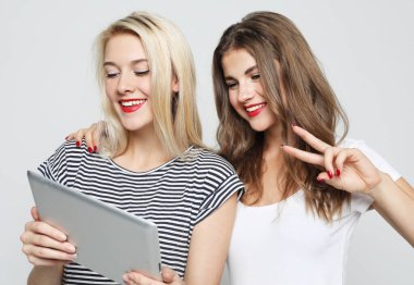 Two smiling female friends taking selfie with digital tablet over white background. Lifestyle and people concept.