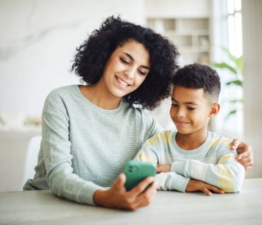 Portrait of young african american mother hold smartphone reading teaching little boy in living room. Lifestyle concept.