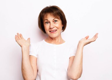 Beyaz tişörtlü, kameraya bakarken şok olmuş olgun bir kadının portresi.