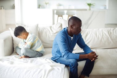 Baba ve oğul birbirlerinden rahatsız olurlar ve sırtlarını kanepeye yaslarlar. Afro ailesi.