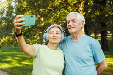 Teknoloji, ilişki ve yaşlılar konsepti - akıllı telefonlu yaşlı çift selfie çekiyor ve parkta sarılıyorlar.