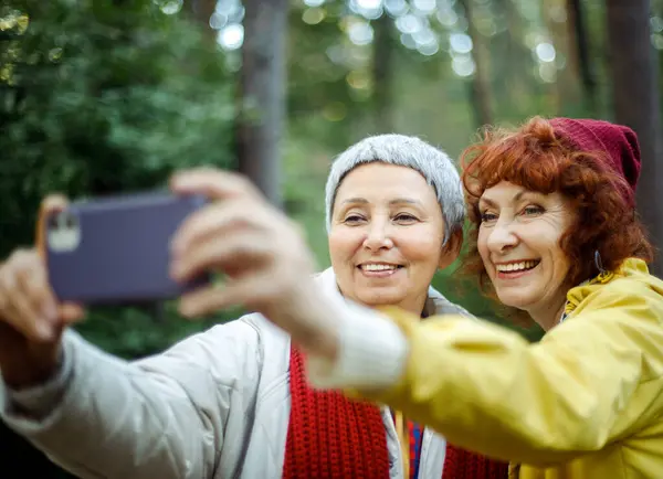 stock image Multiracial elderly women friends having fun during trekking day in to the wood - make selfie with smartphone.