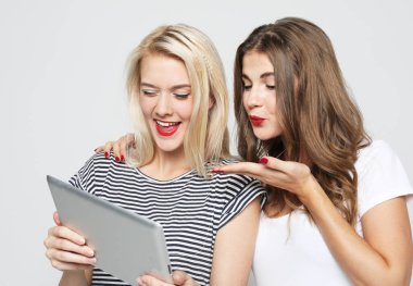 Gülümseyen bayan arkadaşlar beyaz arka planda dijital tabletle selfie çekiyorlar..