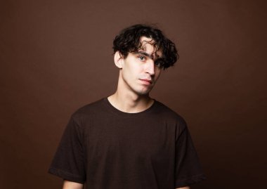 Yakışıklı esmer adam kahverengi arka planda kameraya bakıyor..