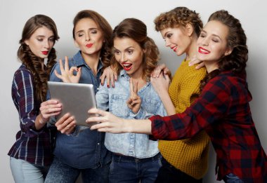 Beş hippi bayan arkadaş gri arkaplan üzerinde dijital tablet kullanıyor.