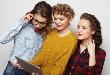 Üç hippi bayan arkadaş gri arkaplan üzerinde dijital tablet kullanıyor.