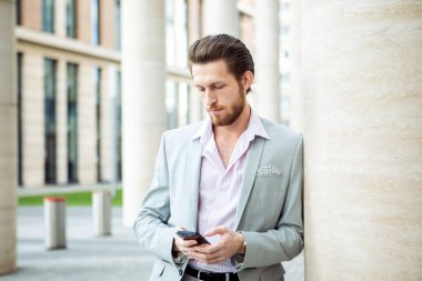 Genç yakışıklı iş adamı şehirde akıllı telefon kullanıyor. İş, insan, tehnoloji ve yaşam tarzı kavramı.
