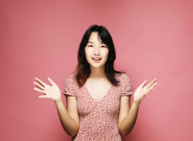 Pembe arka planda elleri açık genç Asyalı kadın, heyecanlı ve mutlu ifade, portre fotoğrafı, stüdyo çekimi, stüdyo ışığı, pembe arkaplan