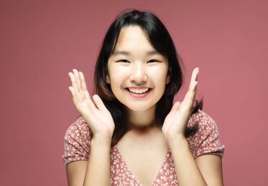 Pembe arka planda elleri açık genç Asyalı kadın, heyecanlı ve mutlu ifade, portre fotoğrafı, stüdyo çekimi, stüdyo ışığı, pembe arkaplan