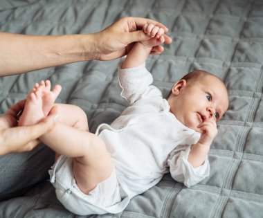 Genç anne, yeni doğmuş bebeğinin ayaklarına yatakta masaj yapıyor. Sıcak renklerde, kapalı bir ortamda, doğal ışık altında, yakın plan el ve vücutta gösteriliyor..