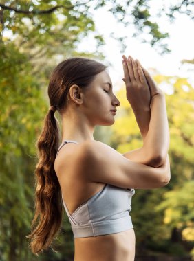 Güzel genç bir kadın yaz günü dışarıda parkta yoga pozu veriyor. Güzel doğal yeşillikleri, bir nehri ve ağaçları olan bir manzara. Bir yaşam tarzı konsepti.