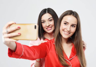 Pijama giymiş, sarılıp gülümseyen iki genç kadın, selfie çekin.