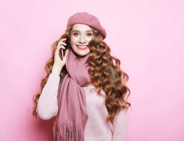 Yakışıklı, kıvırcık saçlı, pembe elbiseli, elinde akıllı telefon tutan bir kadın..