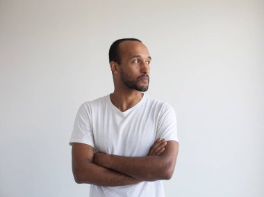 Açık gri arka planda kolları çapraz duran genç Afro-Amerikan adam.