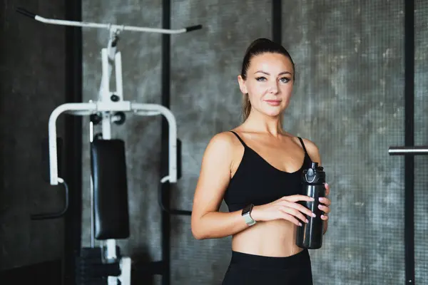 stock image Young sporty smiling woman holding bottle of water. Doing sports at home. Home workout.