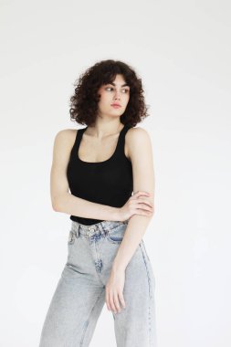 Siyah atletli şık kıvırcık kadın açık gri arka planda poz veriyor..