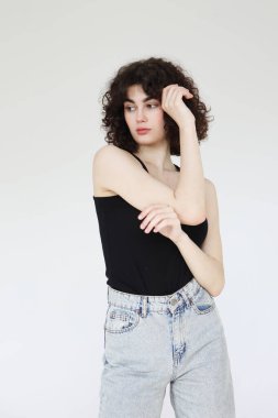 Siyah atletli şık kıvırcık kadın açık gri arka planda poz veriyor..