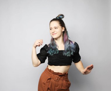 Açık gri arka planda dans eden kıvırcık saçlı neşeli genç kadın, dansın tadını çıkarıyor..