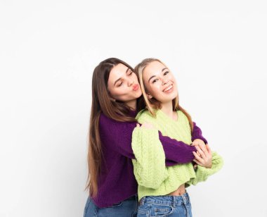 Beyaz bir arka planda gülüp sarılan iki neşeli genç kız arkadaş..