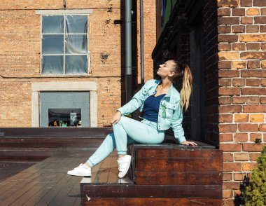 Kot pantolon ve kot ceketli şık bir kadın yaz günü şehirde poz verir..