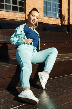 Kot pantolon ve kot ceketli şık bir kadın yaz günü şehirde poz verir..