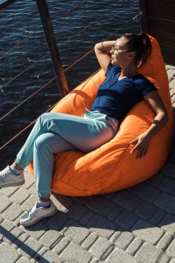 Plajda nehir kenarında dinlenen genç bir kadın şişme fasulye koltukta oturuyor.