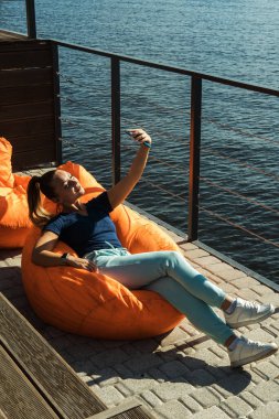 Plajda nehir kenarında dinlenen genç bir kadın şişme fasulye koltukta oturuyor.