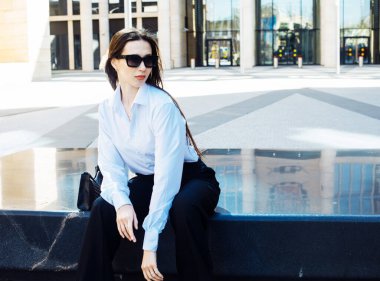 Beyaz bluz ve güneş gözlüğü takmış şık bir esmer kadının portresi. Modern moda. Sokak modası.