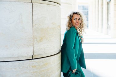 Modaya uygun bir kadın. Sarı kıvırcık saçlı genç bayan model yeşil kıyafetler giyiyor..