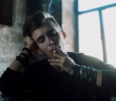 Üzgün, genç, sarışın bir adam karanlık bir odada sigara içiyor..