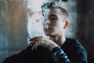 Üzgün, genç, sarışın bir adam karanlık bir odada sigara içiyor..