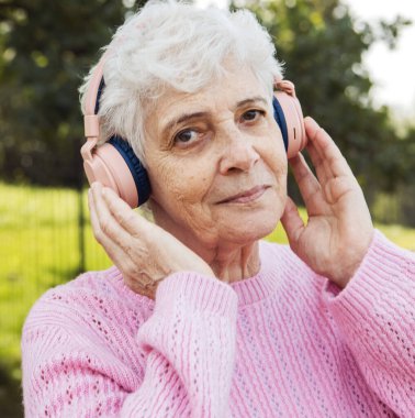 Yaşlı, mutlu kulaklıklı bir kadın parkta müzik dinliyor. Yaşlılık, kıdem ve sağlıkla ilgili kavramlar.