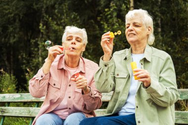 two elderly sisters blowing soap bubbles in a summer park, lifestyle concept. clipart