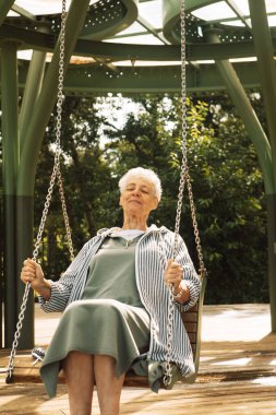 Neşeli yaşlı bir emekli kadın salıncakta sallanarak bir yaz parkında eğleniyor. Yaşam tarzı ve insan kavramı.